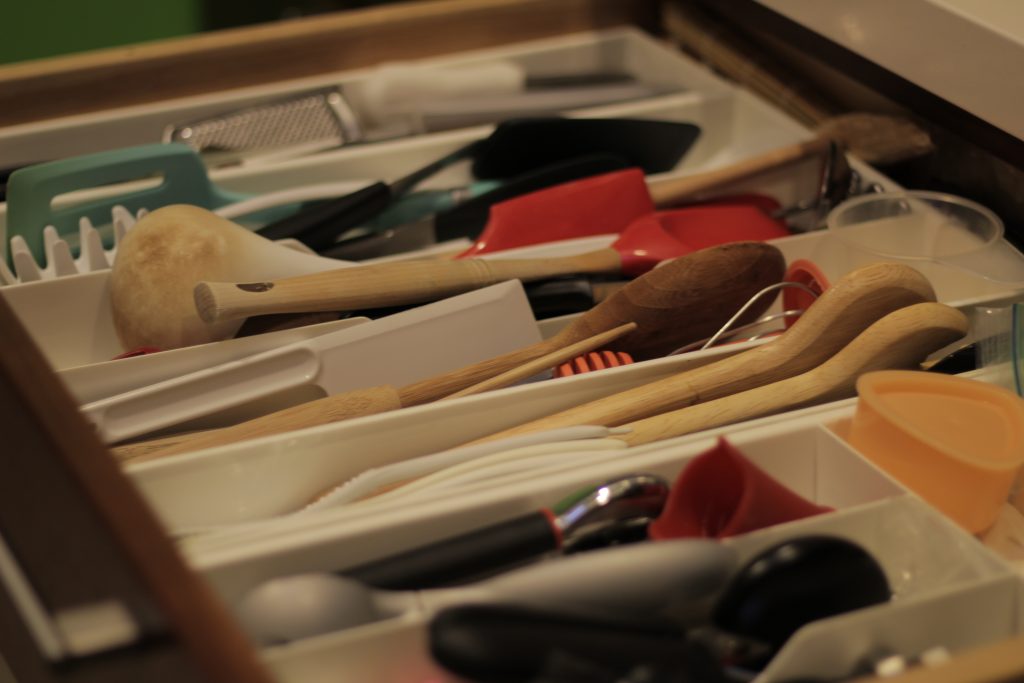 A drawer pulled out with various kitchen equipments- wooden spoons, spatulas, various peelers, etc.
