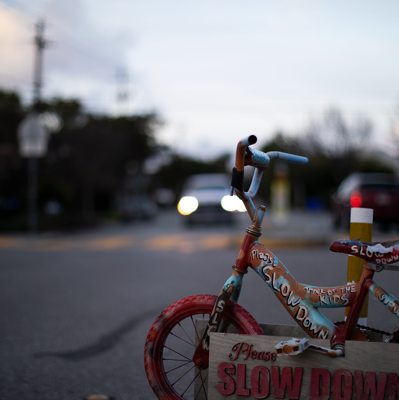 A childs Bike in center frame with the words slow down on it, a cars headlights in the background coming towards you.