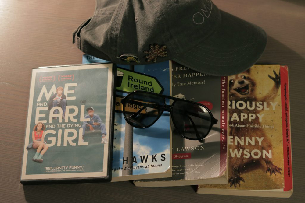 A picture with a movie dvd, three books, a pair of old sunglasses, and a hat with pins on it.