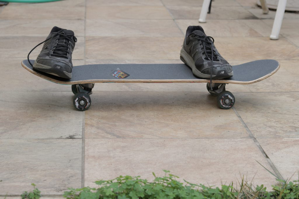 A pear of beat up running shoes placed in a riding stance on a skateboard.