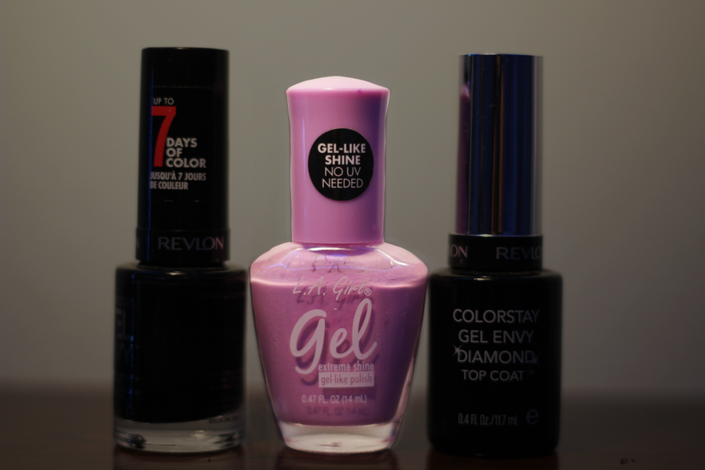 Pink nail polish in the center of the image stands out from the two black nail polishes on either side of it.
