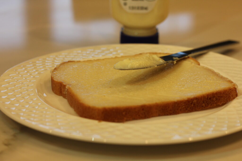 a slice on bread with mayo spread all over it. A butter knife sits on top of the slice of bread.