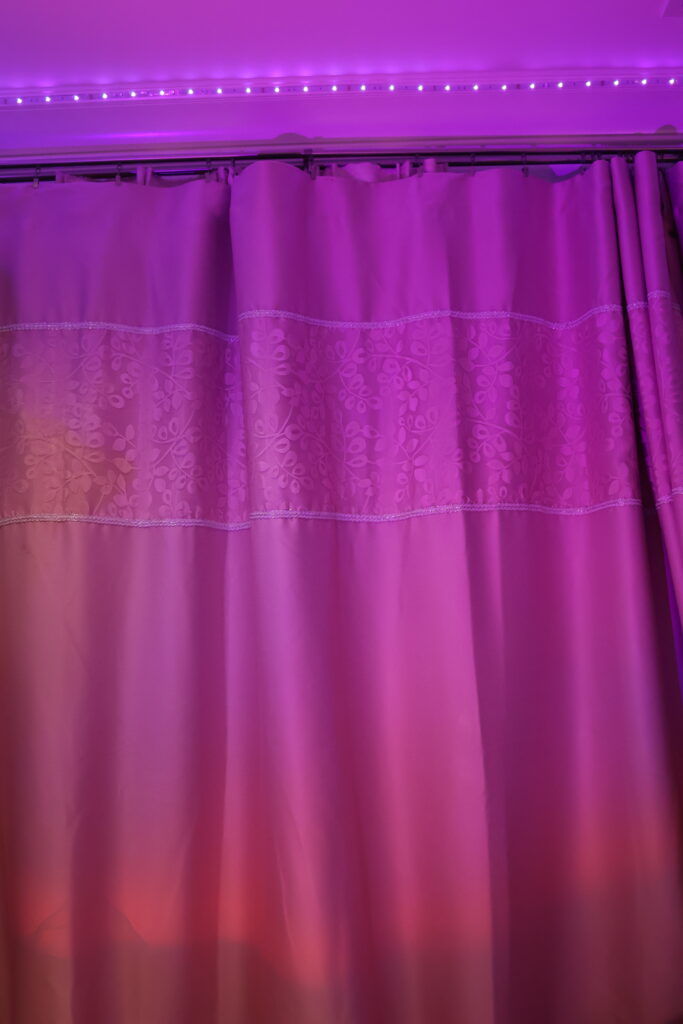 a pink floral curtain with pink lights on the ceiling and pink lights shining at the curtains
