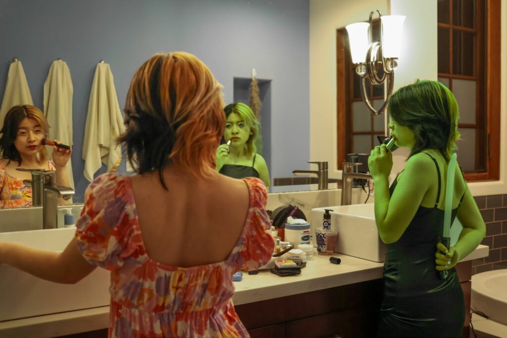 two Fionas standing in front of a mirror, one green and with a knife behind their back