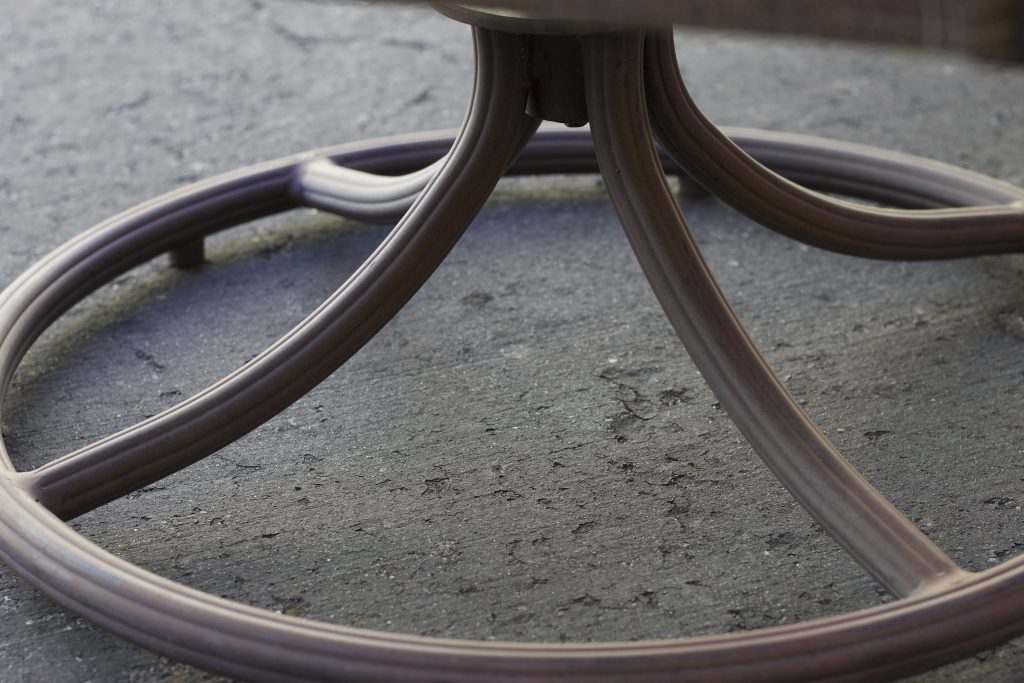 This image portrays the bottom of a metal outdoor chair it is circular at the bottom with pieces of curved metal to support the center forming triangles