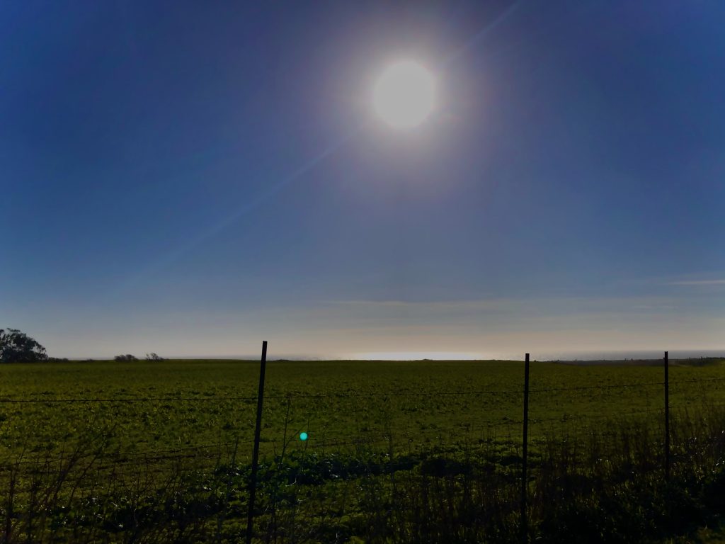 This is an image of a landscape view framed with a fence in the front and the sun centered up top in the middle