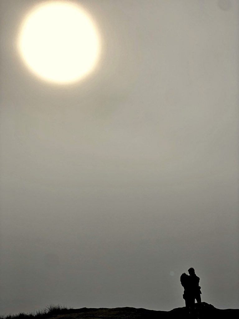 A silhouetted couple in front of a huge sun. 