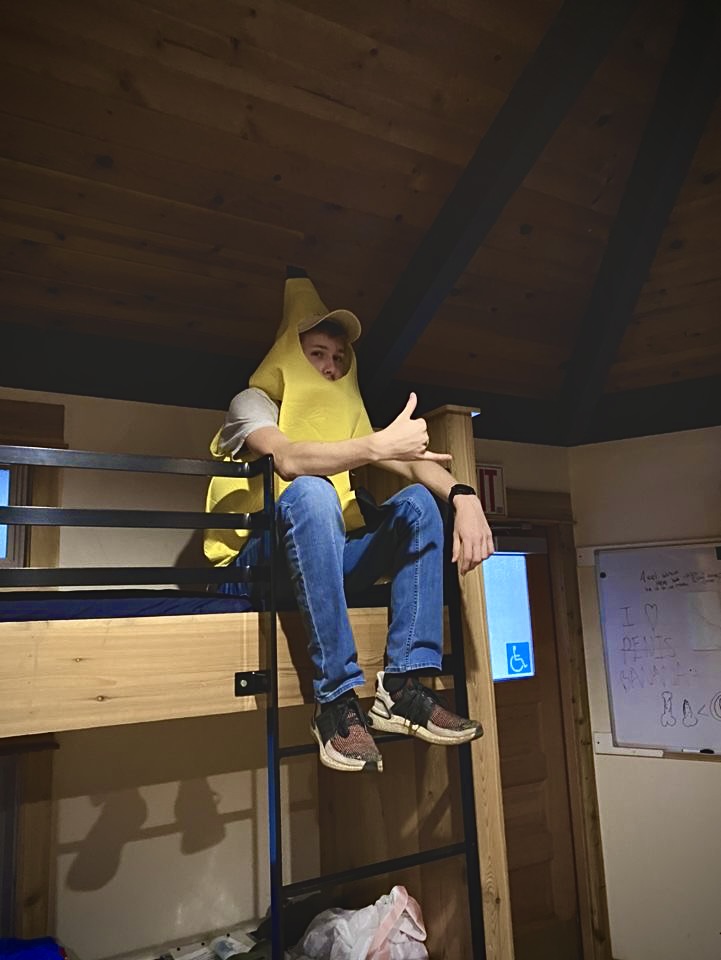 A man sits on the top bunk of a cabin bed in a banana costume. 