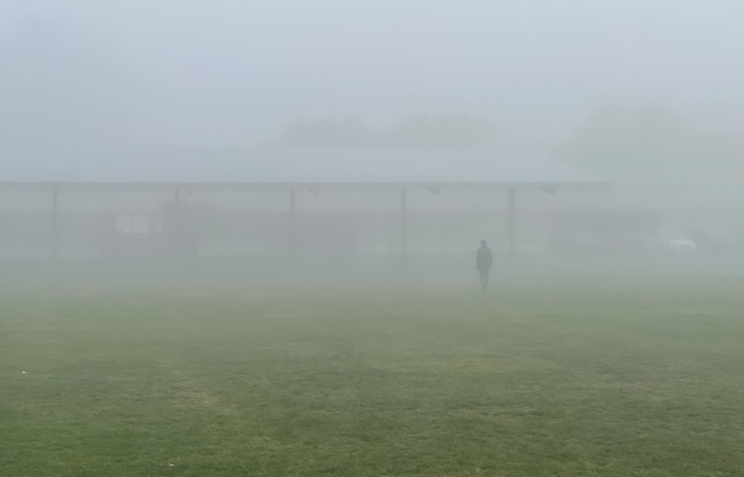 A man walks through a field of fog to a school. 