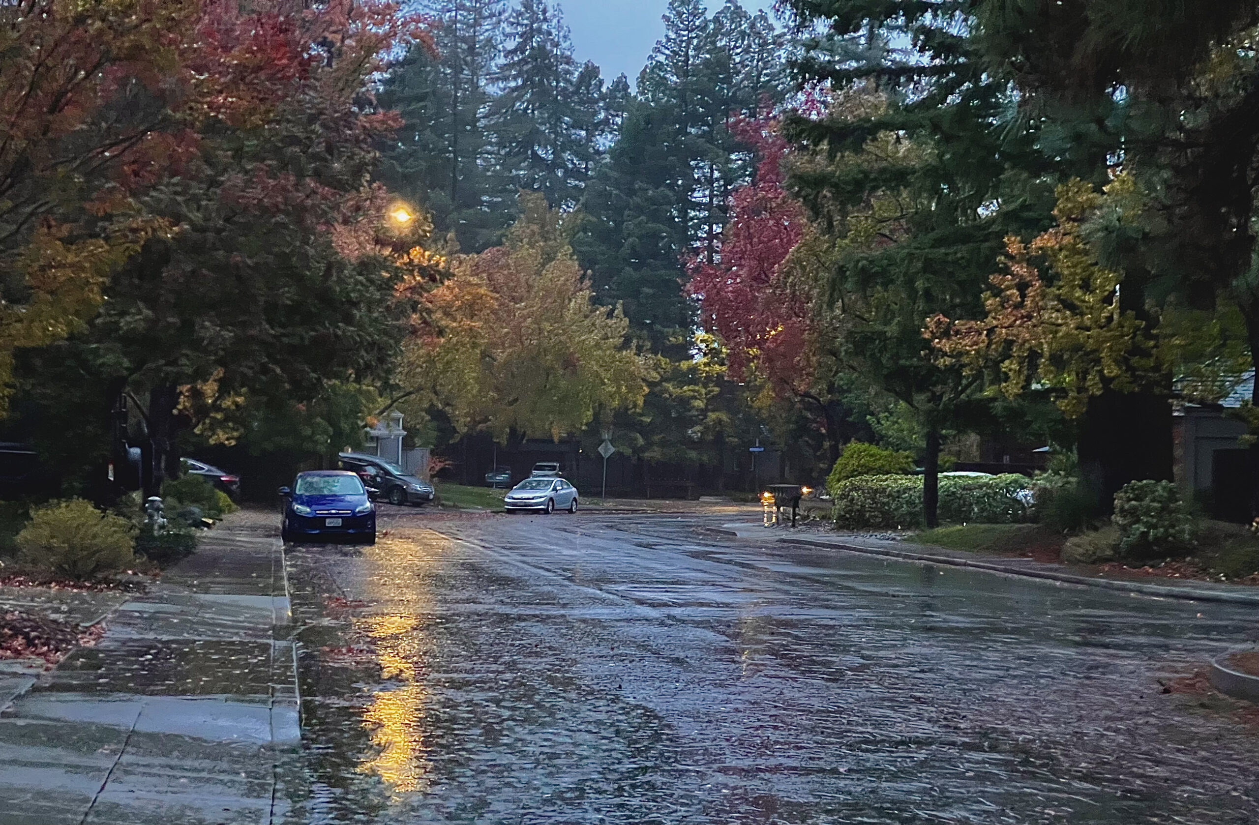 A rainy day suburban street with a beam of light and single car on the left. 