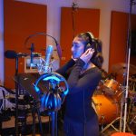 Saumya holding her headphones while singing in awesome blue lighting