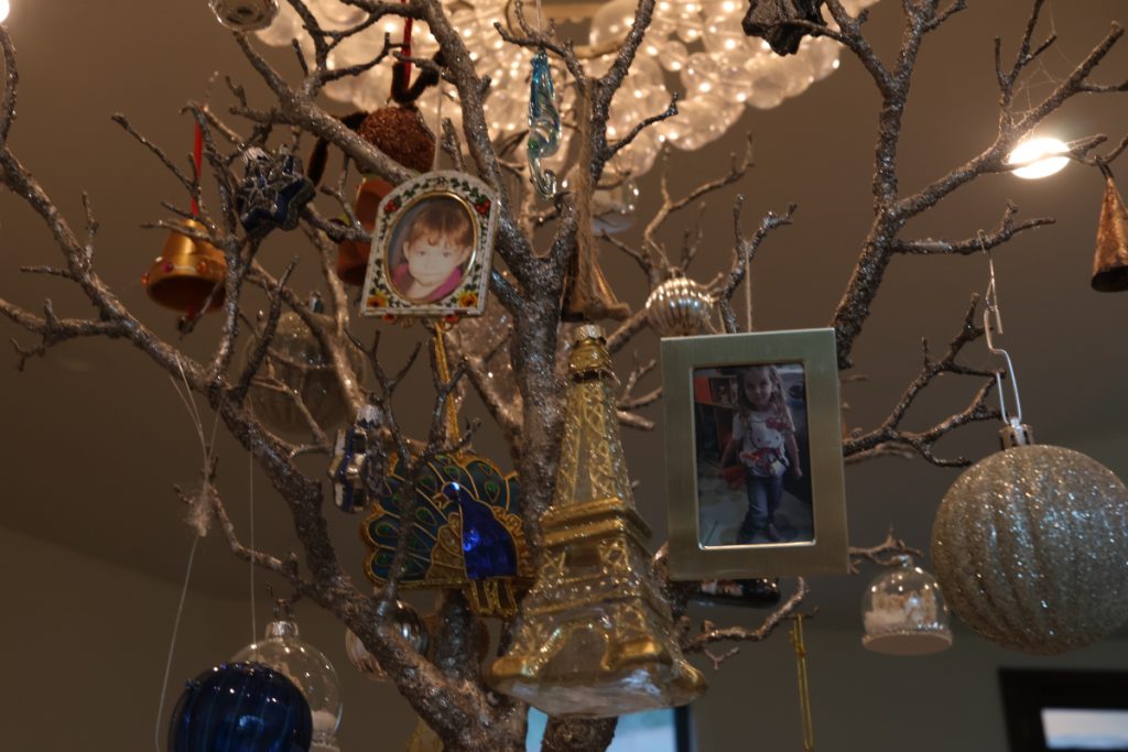 Silver sparkling branches adorned in various holiday ornaments, large light gives a halo effect.  