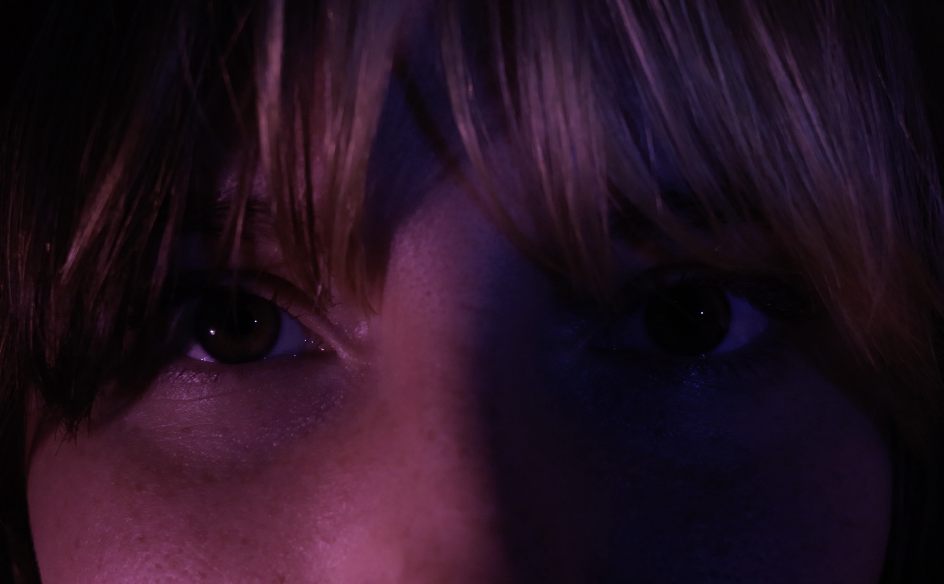 Brown eyes lit by pink light on the left and dark blue on the right. 