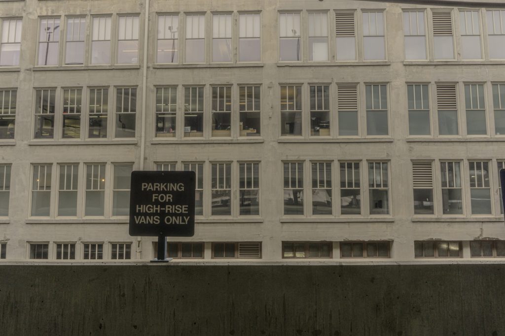 There is a balocny in the lower third of the photo with a sign reading "parking for high-rise vans only". The balcony looks out at a wall of windoes from an apartment building. 