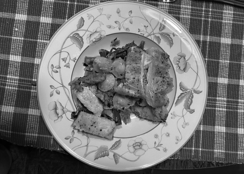 A black and white photo of a plate of chicken and pasta placed on top of a striped placemat. 