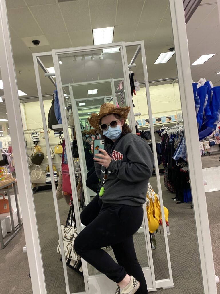 A girl in a straw hat poses in front of a mirror wearing sunglasses. It's clear she's trying to be silly. 