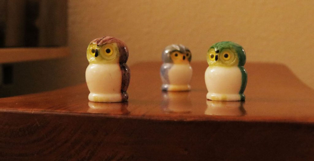 Three alabaster owls on a stool, each a different color.