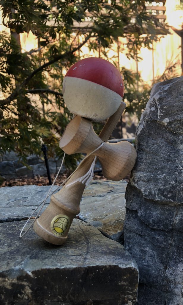 Kendama leaning on a rock. Red and white ball, wooden stick.