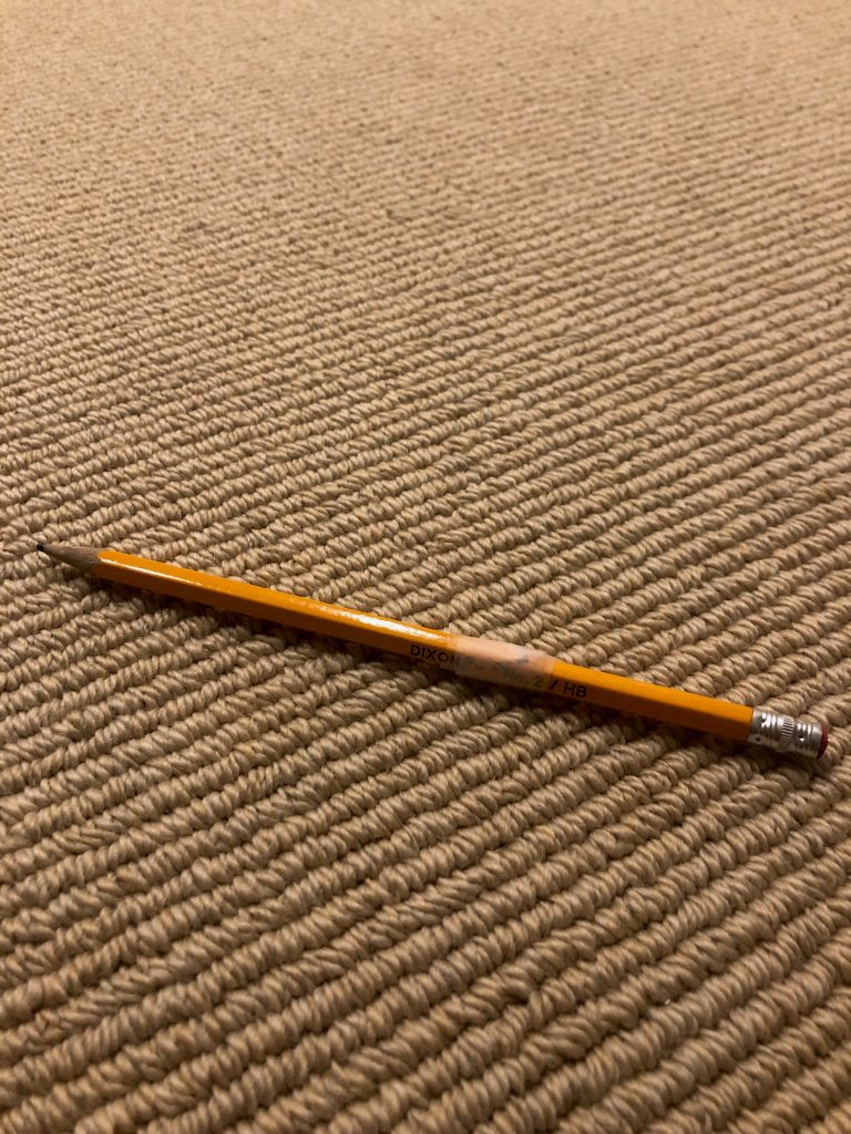 Broken orange pencil. Clear tape holding it together on carpet.