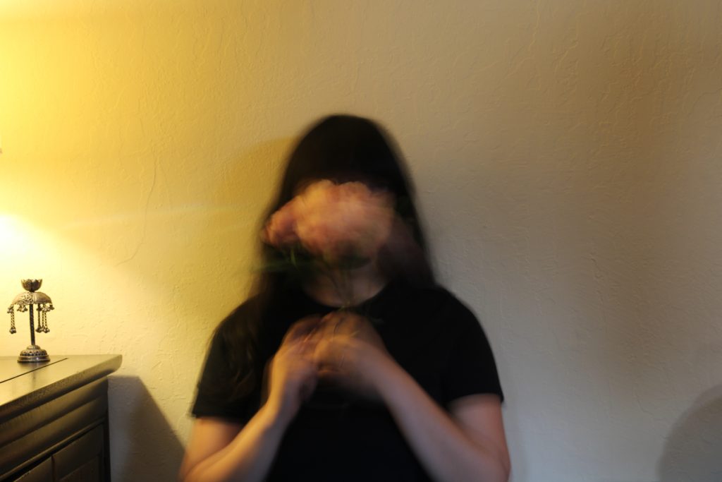 Faceless photo of girl with pink flower bunch in front of face and warm lighting coming from the left side.