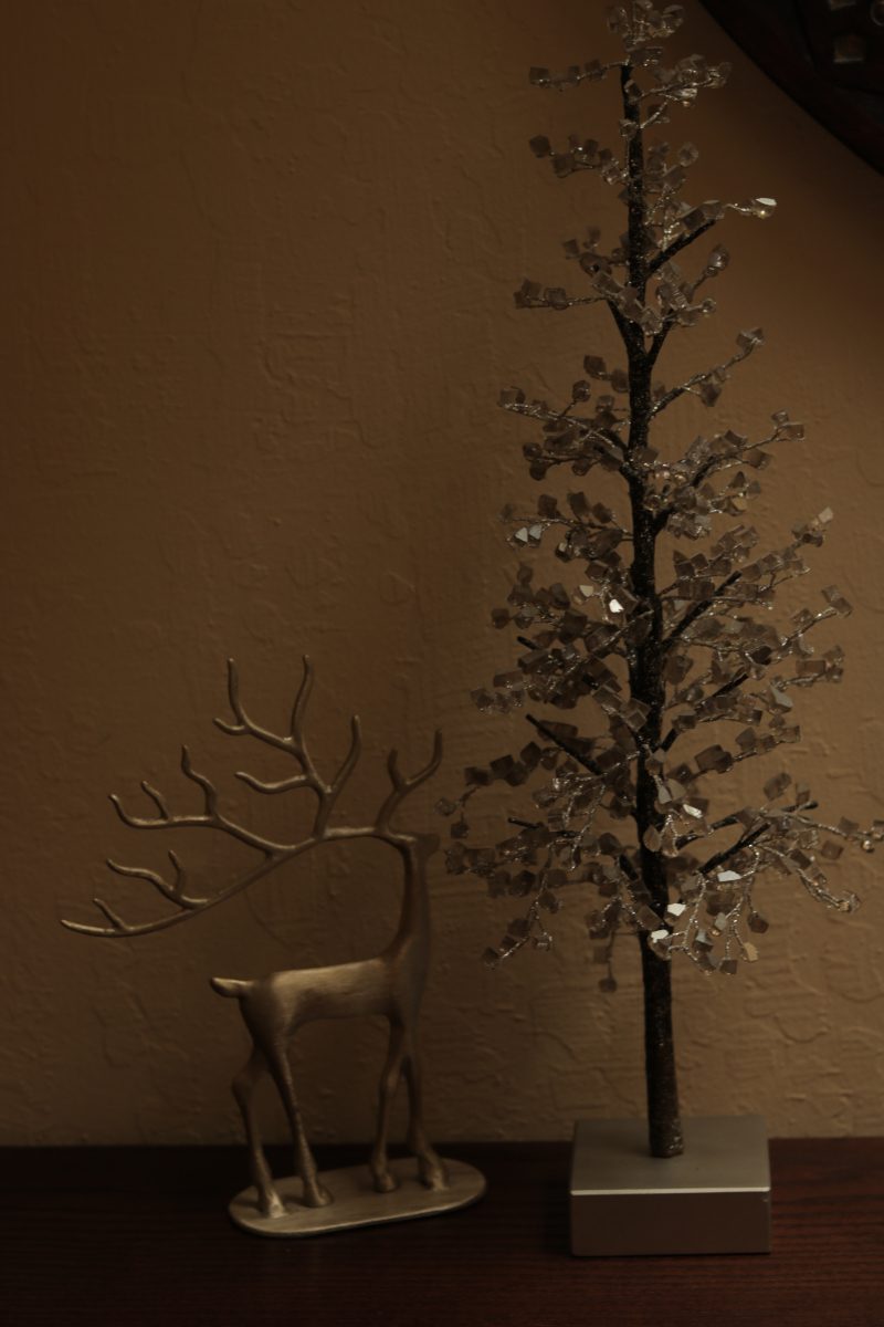 Photo of a gold reindeer and crystal tree sitting on top of a dark brown wood table. 