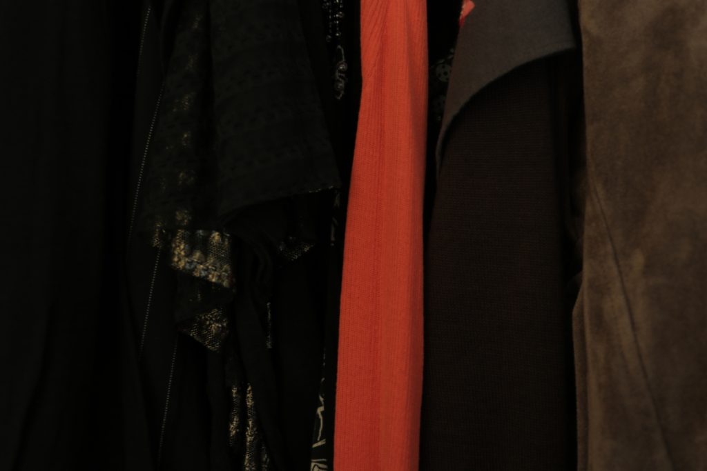 Photo of closet. Close up of dark brown and black clothing with bright red cardigan in the middle of dark clothing. 