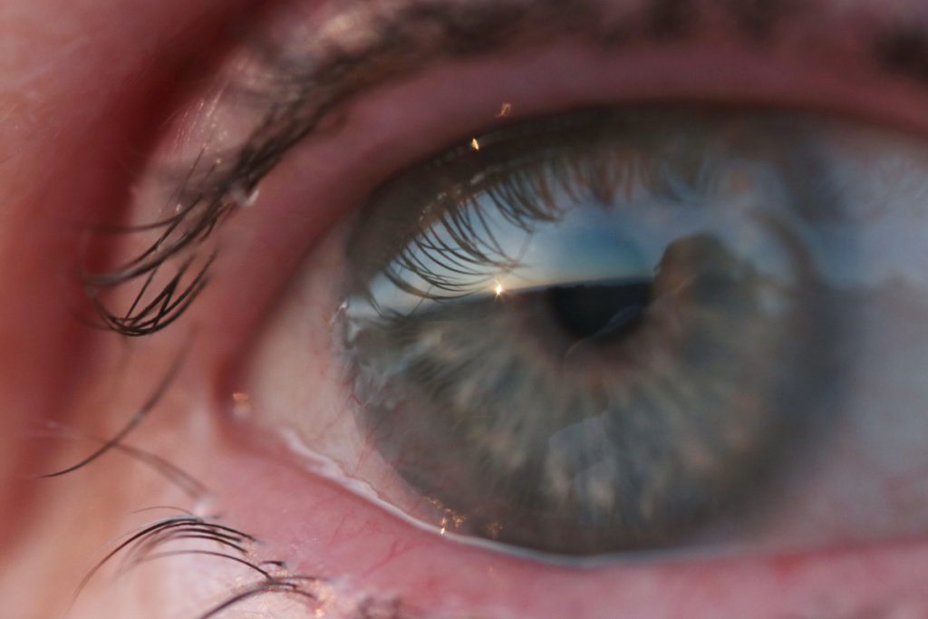 Up close photo of an eye with a reflection of a sunset across half of the iris.