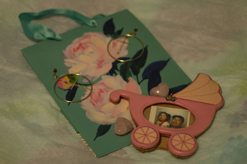 a birthday bag with flowers with a pair of hoop earrings with a cross and to small heart rose quartz and a pink stroller frame with a crown with an image of a little girl and dad with hat