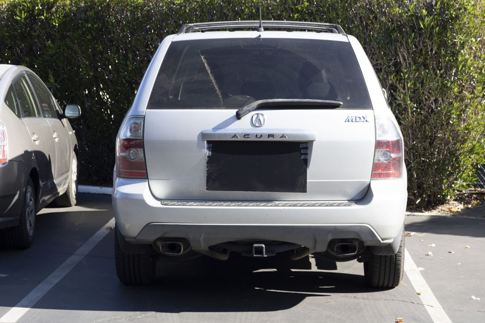 The back of a silver SUV. The license plate is covered with a piece of black plastic.