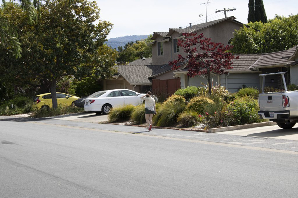 A person walking on the sidewalk, in the suburbs.