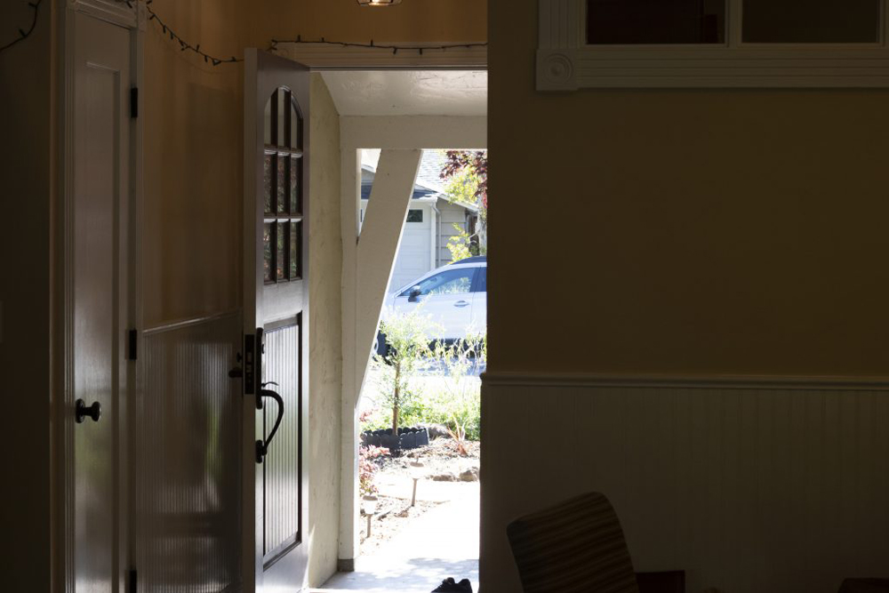 The open front door of a house as seen from inside. Through the door one can see plants and trees.