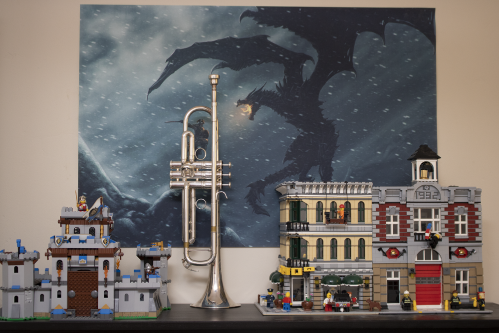 An image of a trumpet and some lego buildings in front of a poster of Skyrim, in which a man in armor is fighting a dragon on a snowy mountaintop.