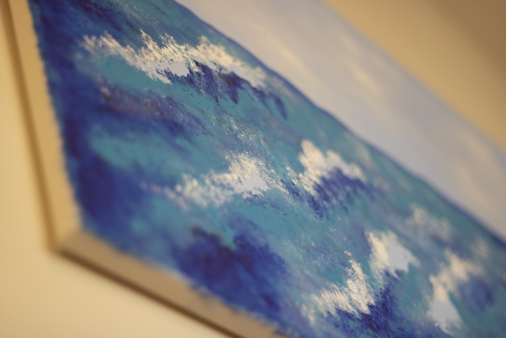 A picture of a painting, as seen from the bottom left corner. The painting is of ocean waves, and the color palette consists of various blue hues and white. 
