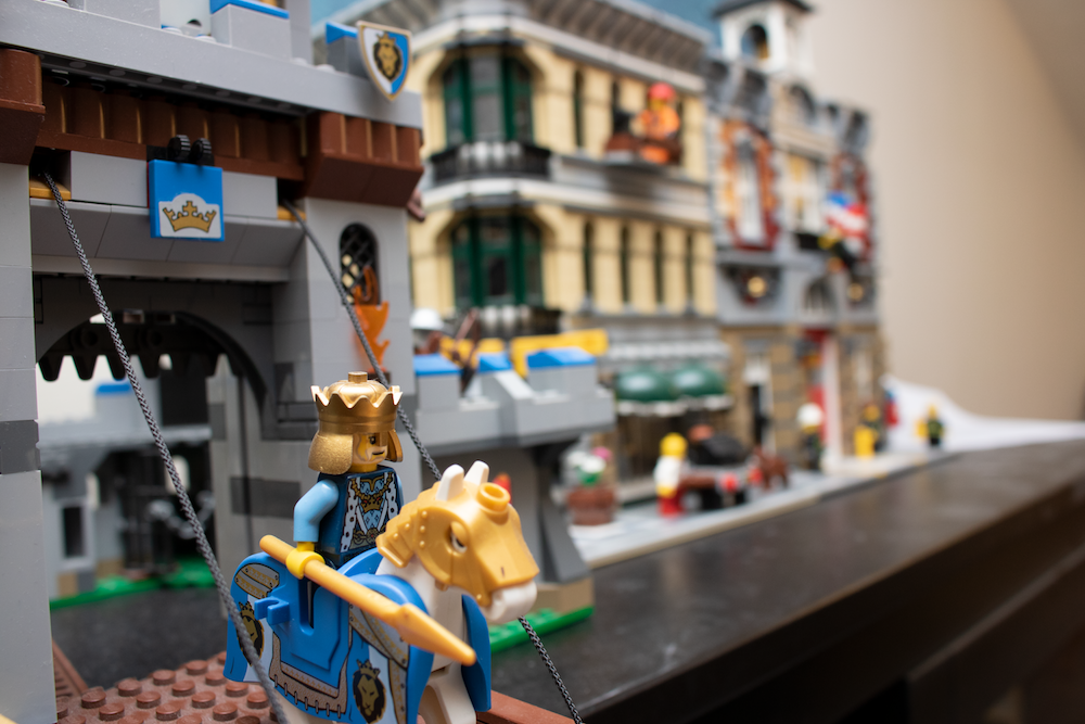 An image of some legos. A LEGO king, riding his horse, stands on the drawbridge of his castle. 