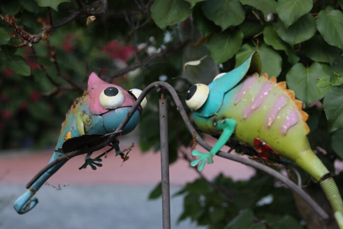Two colorful gecko garden decorations in front of a large bush