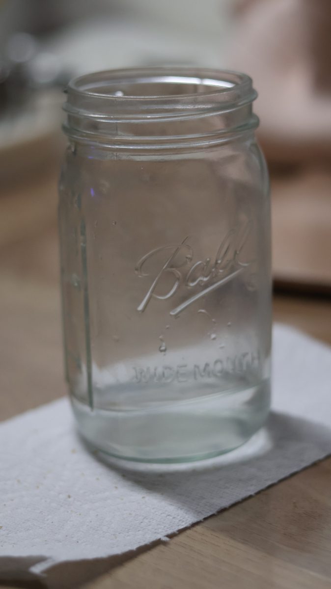 A photo of a mason jar with a little water sitting on a napkin on the table, jar takes up majority of frame