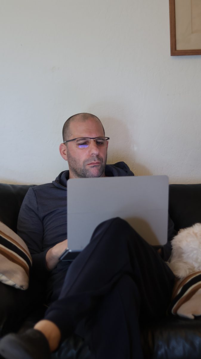 Good looking bald man sitting on the couch and working on his computer by himself. 