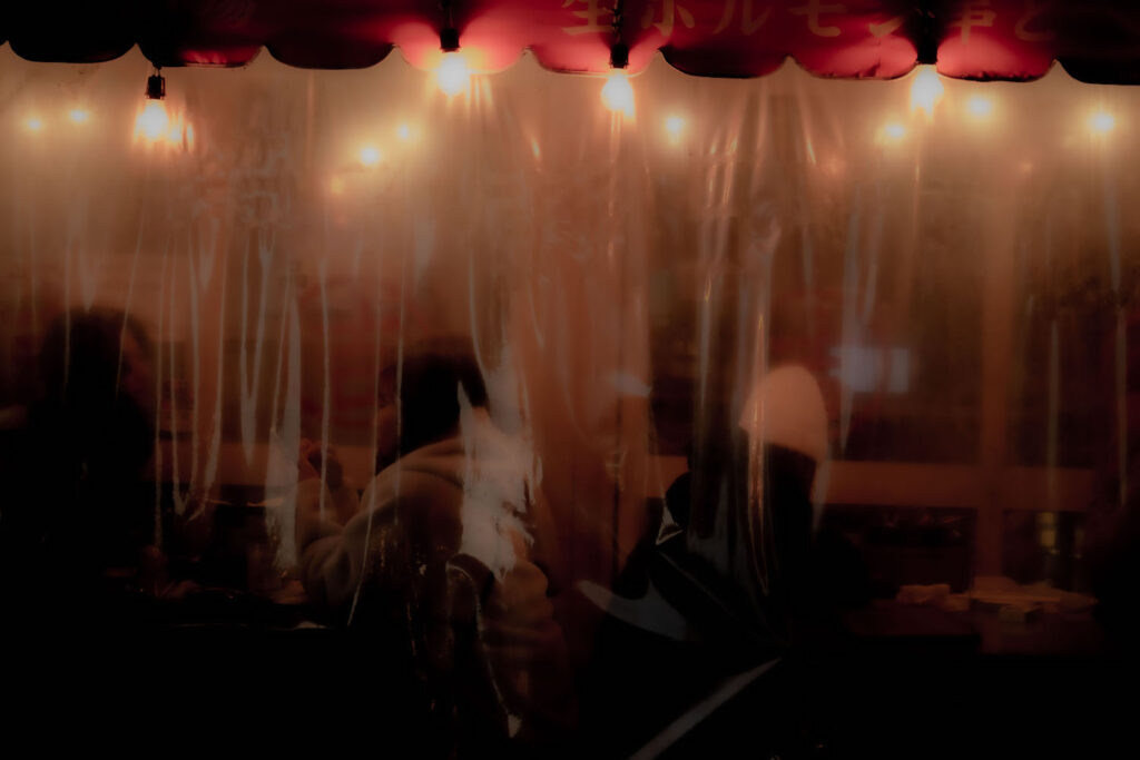 photo of several figures sitting behind a clear plastic curtain at a restaurant.