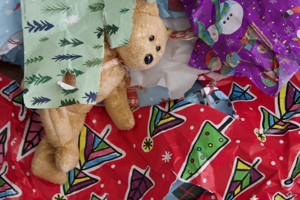 Teddy bear lying forlornly among the bright patterns of crumpled up wrapping paper