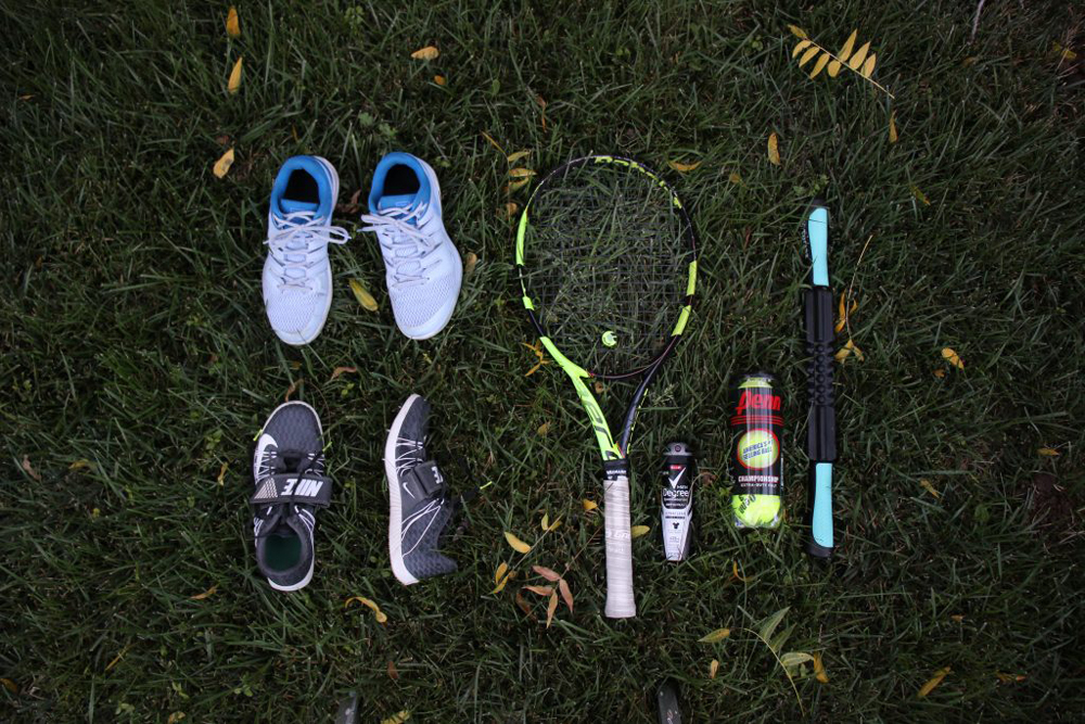 Photo of a self portrait. The photo shows various sports equipment including shoes, a racket, a roller, track spikes, and others. All of this is laid out on grass. 