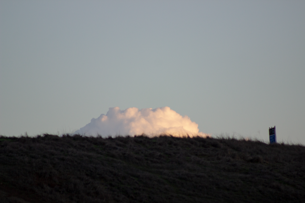 The image pictures a meadow/hill with a vivid, pinkish cloud behind it.