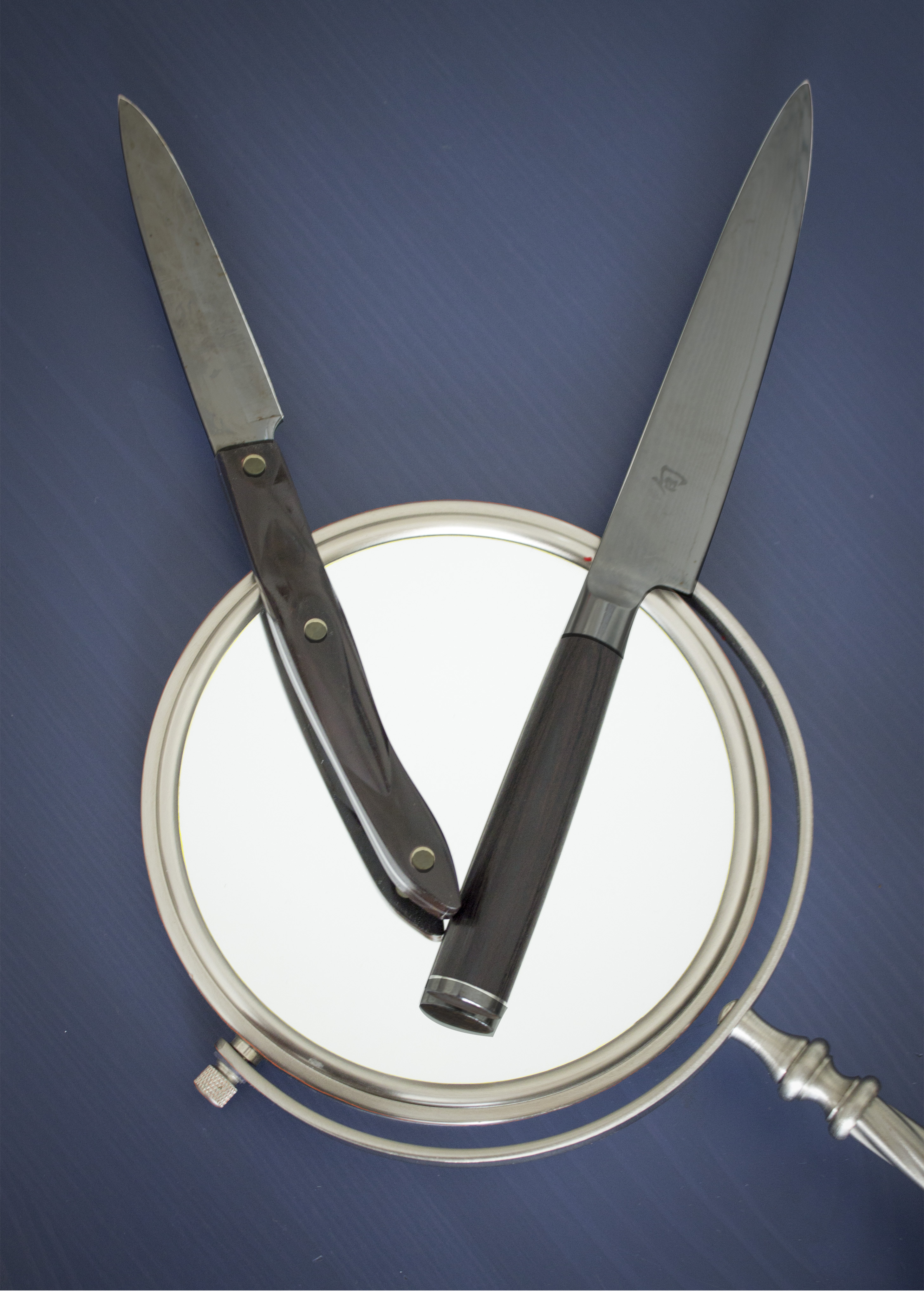 A mirror with 2 scissors over it like the hands of a clock. It is laying on a dark blue table.