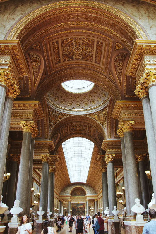 The inside of a museum in Italy with golden embellishments and posts with a detailed ceiling.