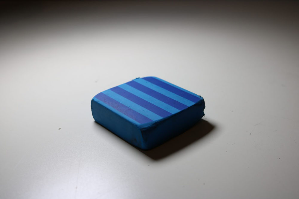 A picture of a blue eraser on a white tabletop.