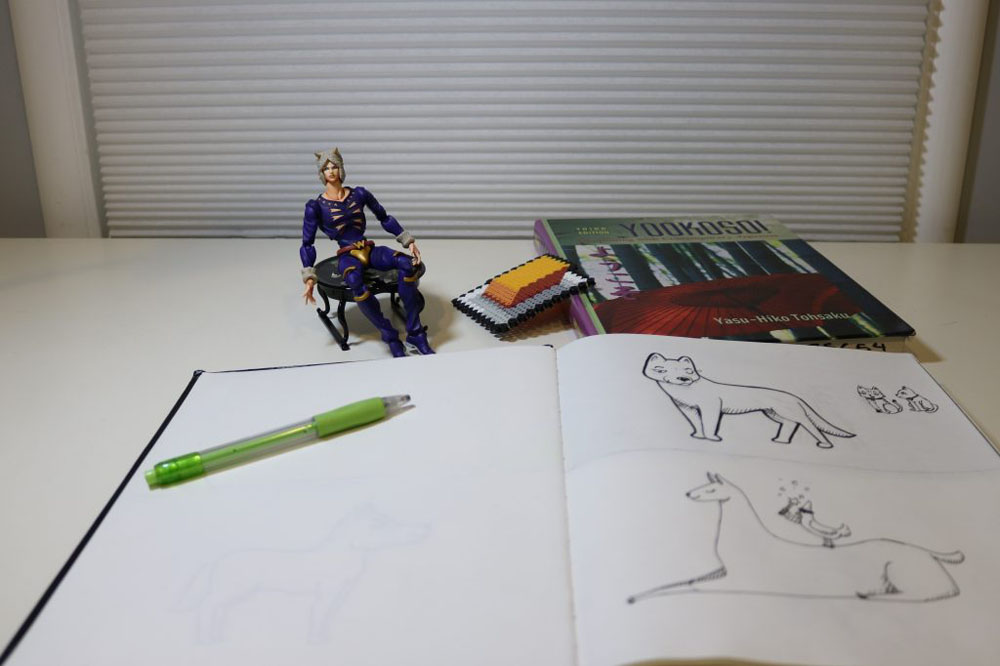 A photo of a sketchbook, Japanese textbook, Perler Bead creation, and a figurine.