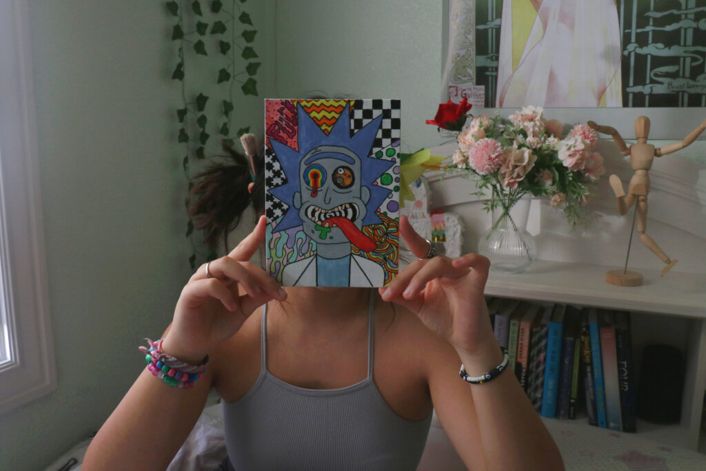 A picture of me in my room with a painting of Rick from a show called Rick & Morty covering my face. The painting over my face is filled with a bunch of crazy patterns.
