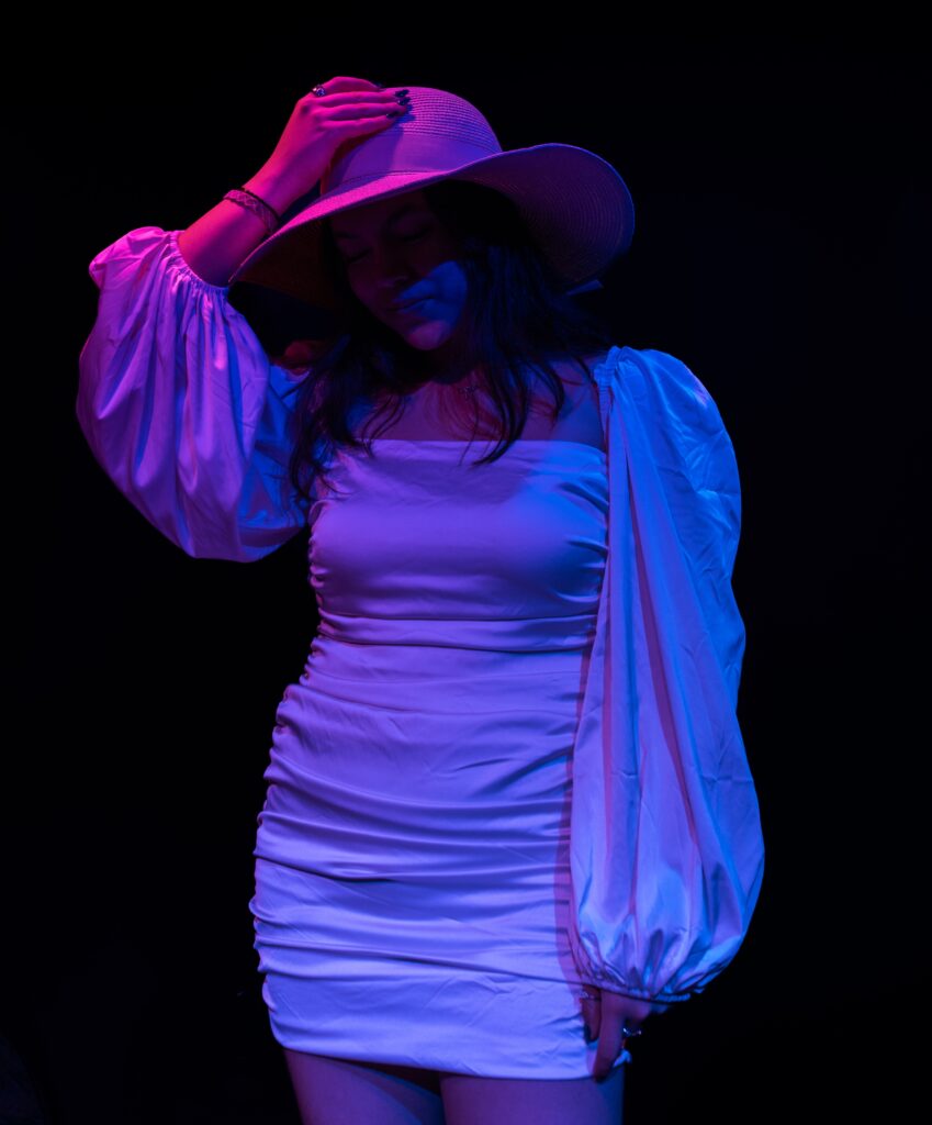 a girl in a white dress with pink and blue lights with a hat shadowing her face.