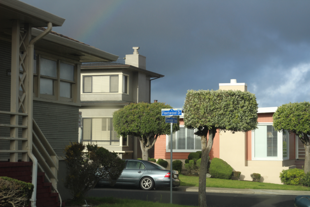 a neighborhood view with a rainbow in the background and a street sign saying "Fleetwood Dr"