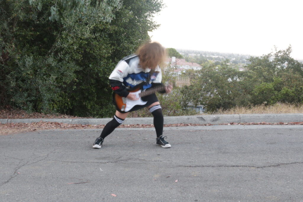 Stella is playing her guitar outside in the road. Her motion is heavily blurred from the very long exposure length of the camera.
