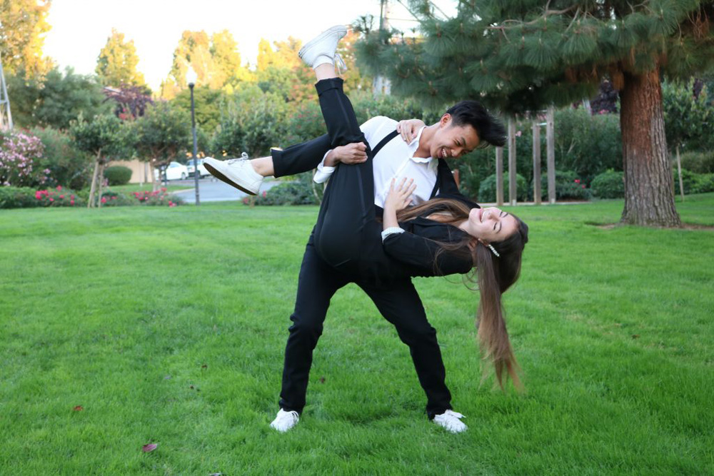 The photo is a girl and a boy dressed up for a homecoming dance for high school. The boy is holding the girl up in the air and flinging her around.